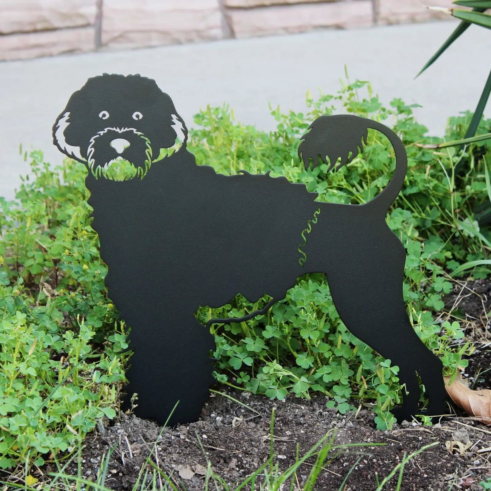 Black metal silhouette of a Portuguese Water Dog, detailed with green accents, nestled in green ground cover.