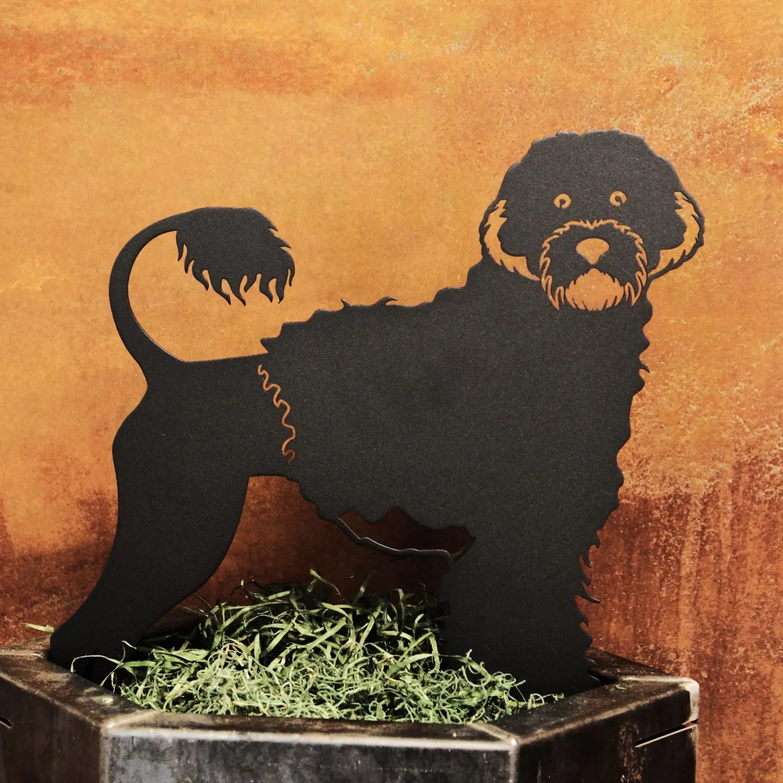 Black metal silhouette of a Portuguese Water Dog standing on decorative moss, showcasing its curly fur and playful stance.