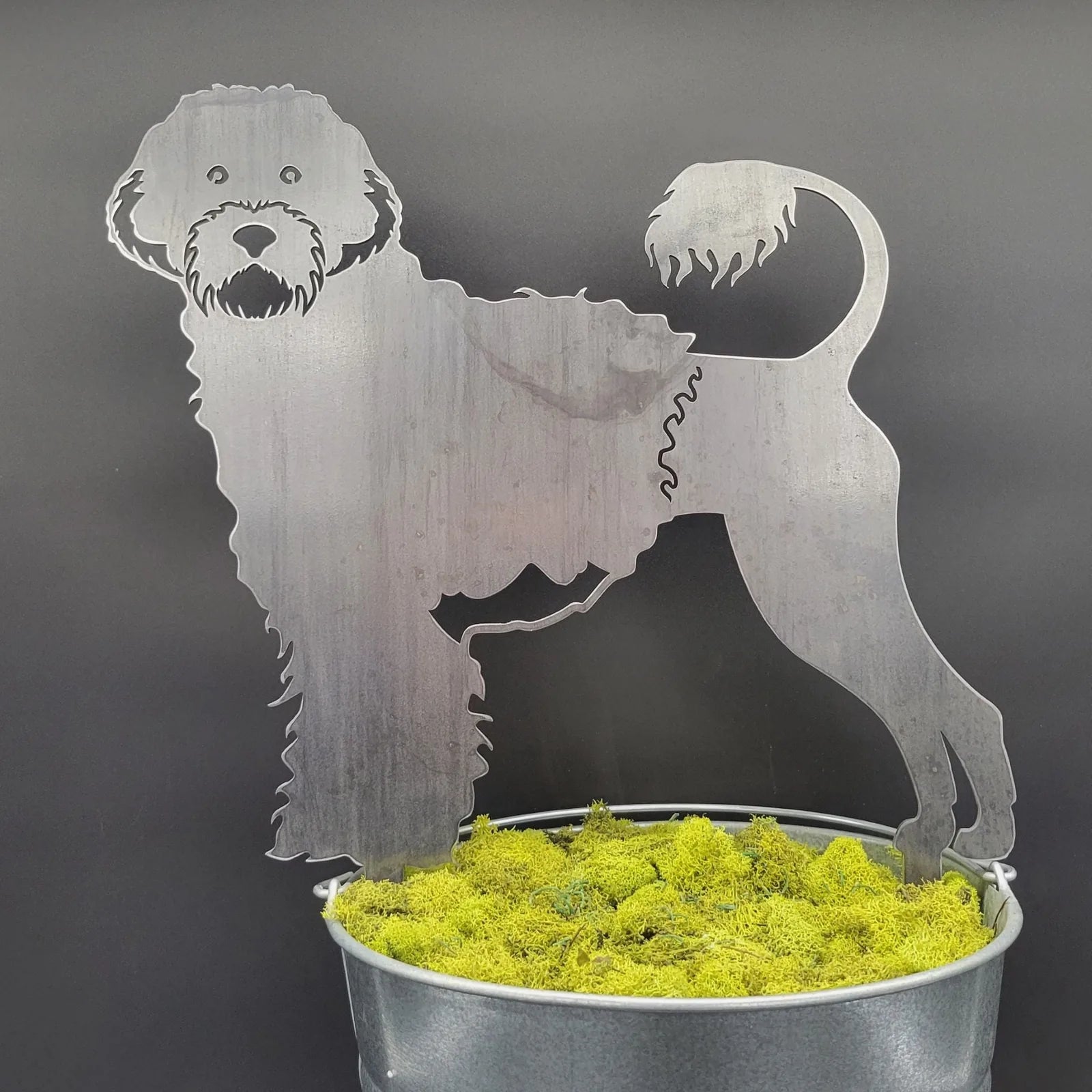 Portuguese Water Dog metal silhouette in weathered steel, standing amidst green moss in a metallic planter.