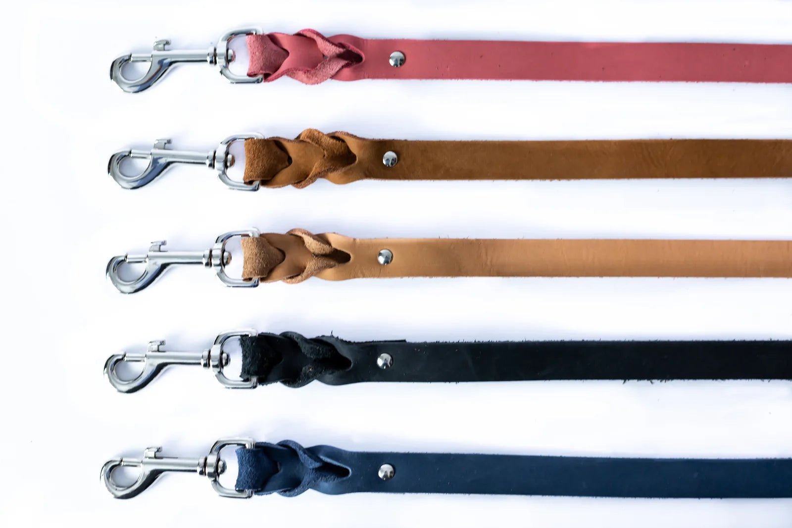 Braided leather dog leashes in coral, tan, black, and navy with stainless steel clips, showcasing quality craftsmanship.