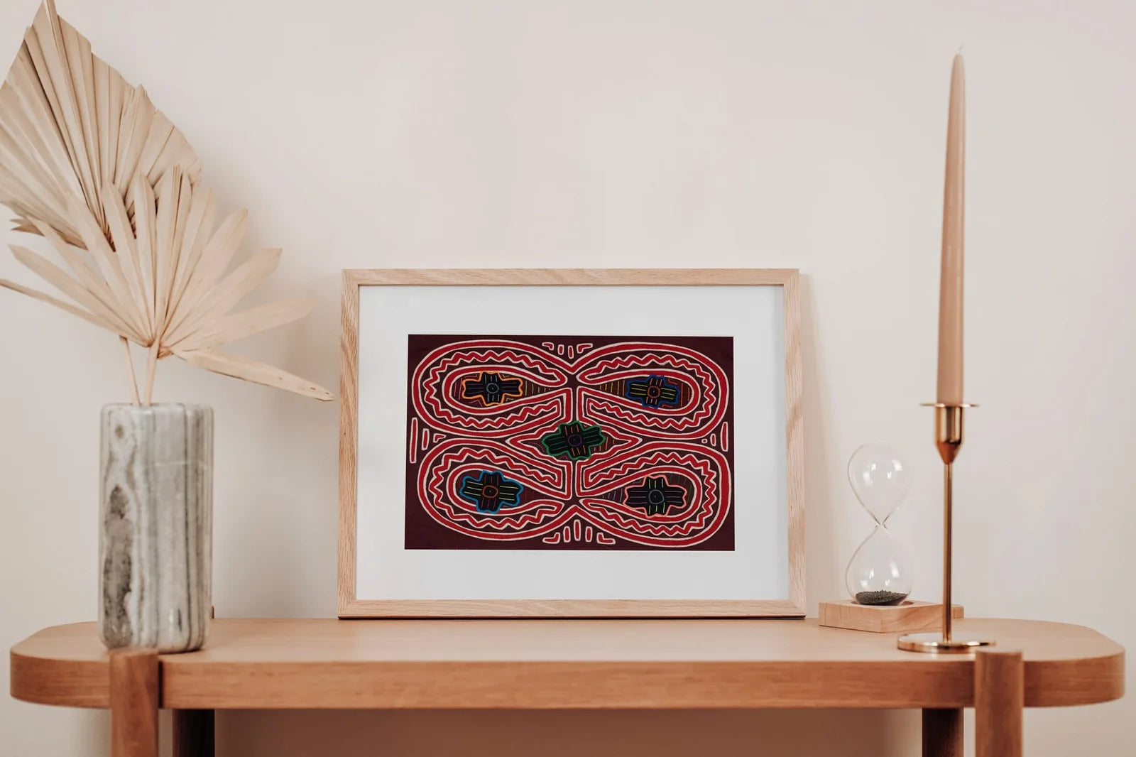 Colorful hand-stitched Mola textile with geometric patterns, framed and displayed on a minimalist wooden shelf.