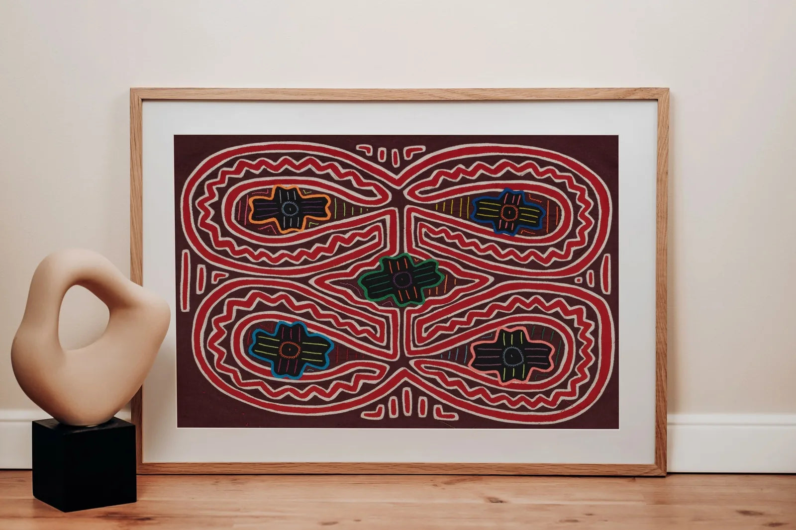 Colorful hand-stitched Mola tapestry featuring geometric patterns on a deep maroon background, framed with a wooden border.