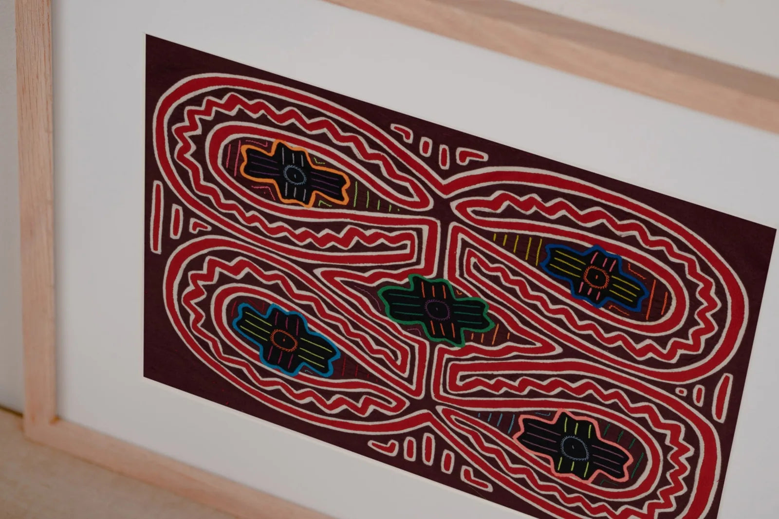 Hand-stitched Mola tapestry featuring vibrant geometric patterns in red, yellow, green, and blue on a dark background.