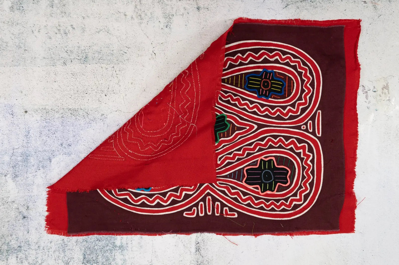 Hand-stitched Mola tapestry in red and burgundy with colorful geometric designs, showcasing fair trade craftsmanship.