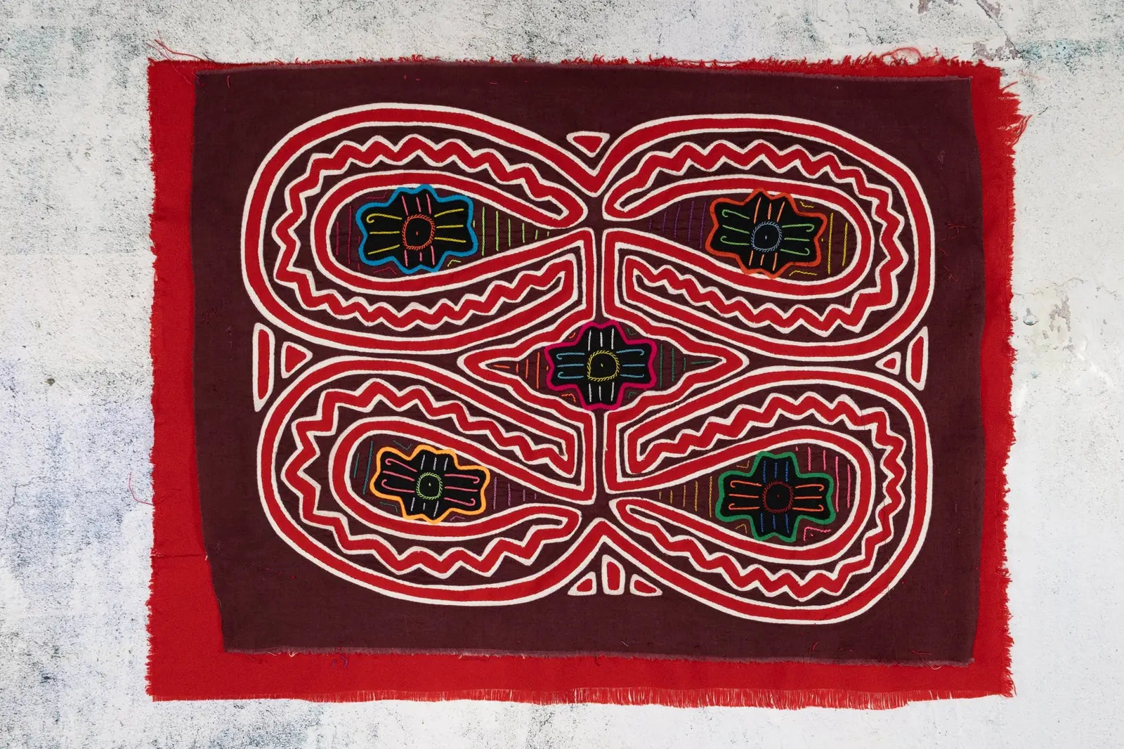 Hand-stitched maroon tapestry featuring colorful floral designs and geometric patterns, showcasing traditional mola artistry.