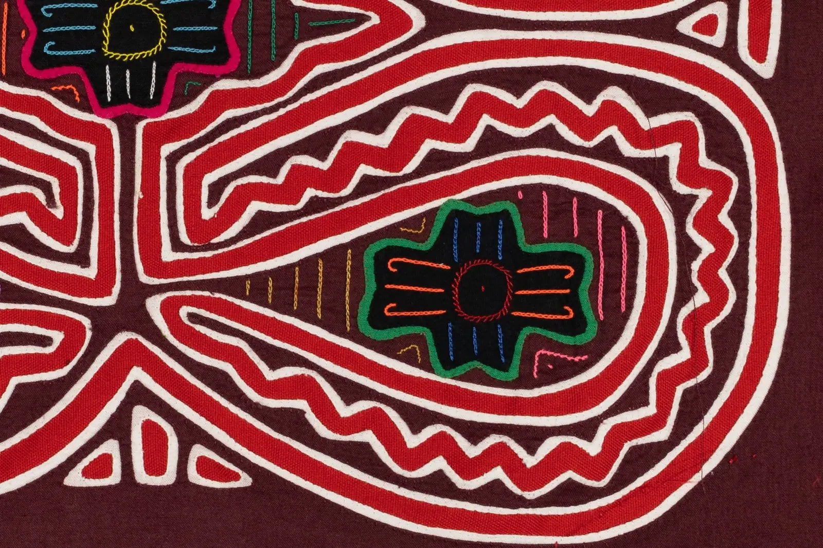Colorful hand-stitched Mola featuring intricate red, white, and black patterns with floral and geometric designs.