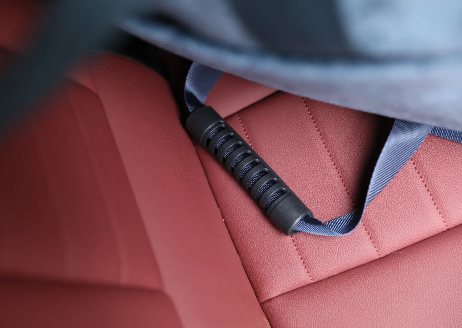 Close-up of the Puff Guard Dog Car Seat’s adjustable safety strap resting on a textured, red car seat.