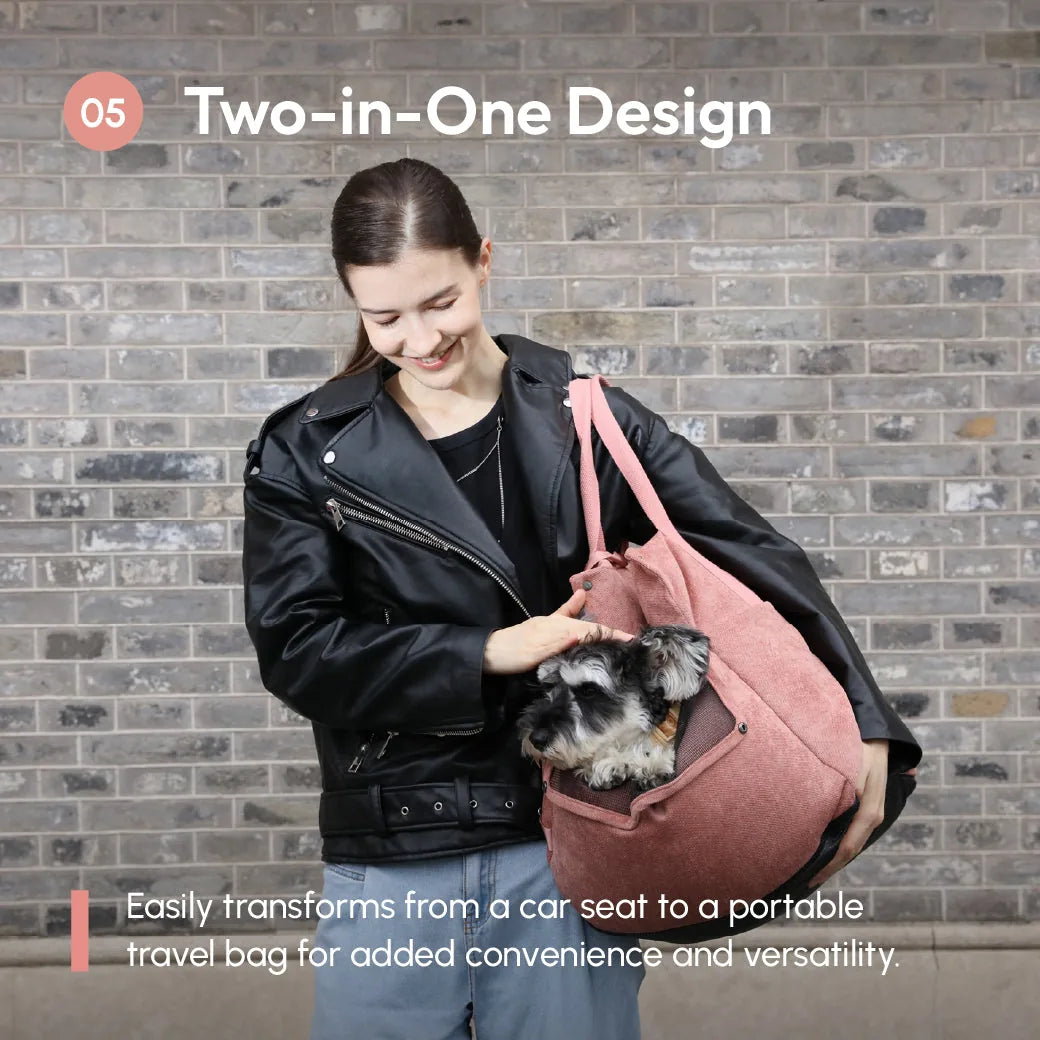 Woman in a black jacket holds a pink car seat bag with a small dog, showcasing the two-in-one design for travel.