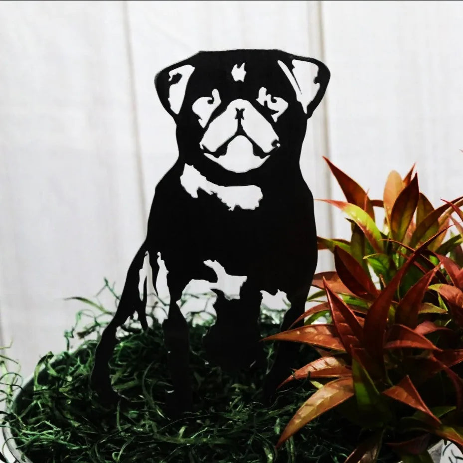 Black metal silhouette of a Pug, set amidst lush greenery and colorful plants, showcasing stylish outdoor decor.