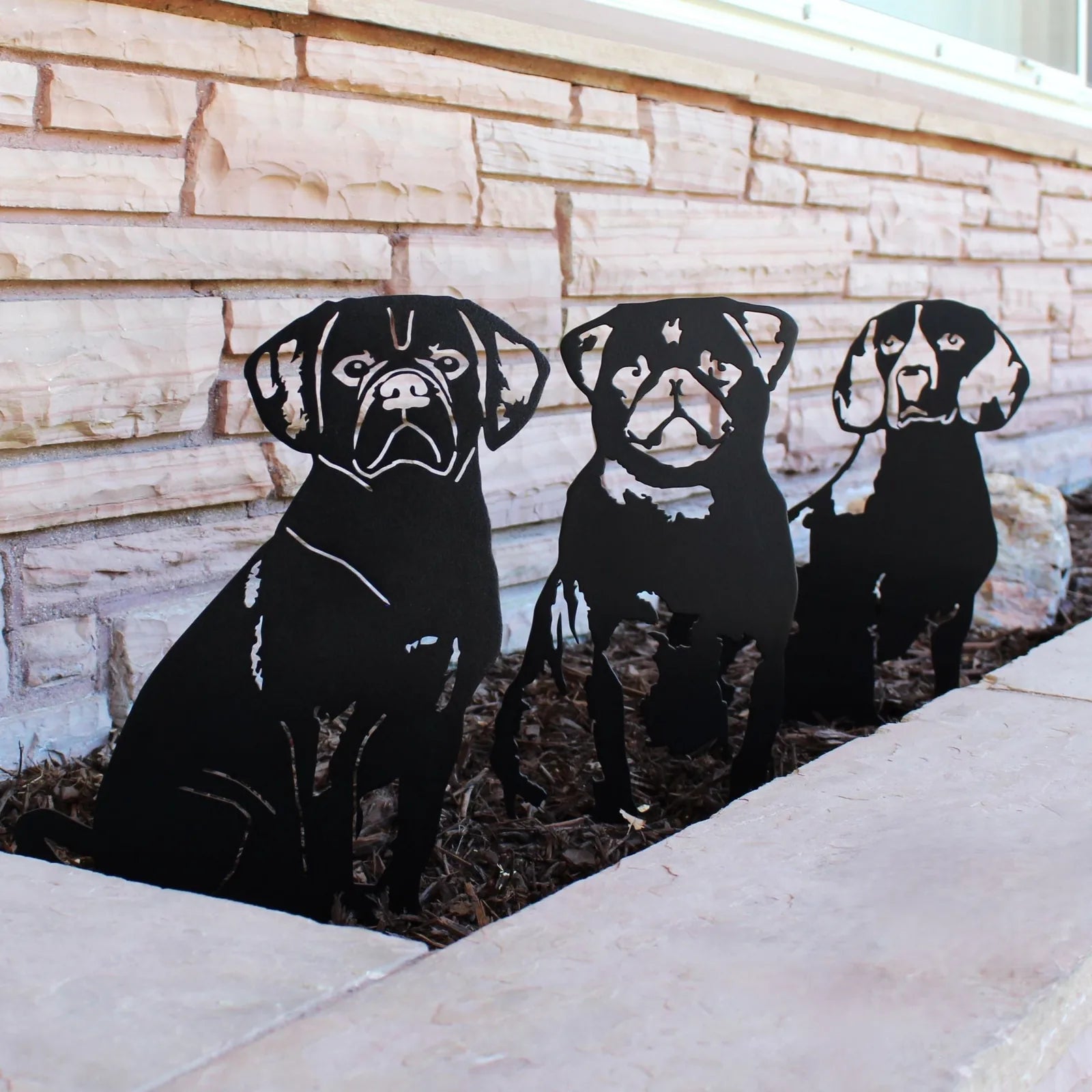 Black metal silhouettes of three dogs, set against a stone background, showcasing a stylish dog-themed outdoor decor.