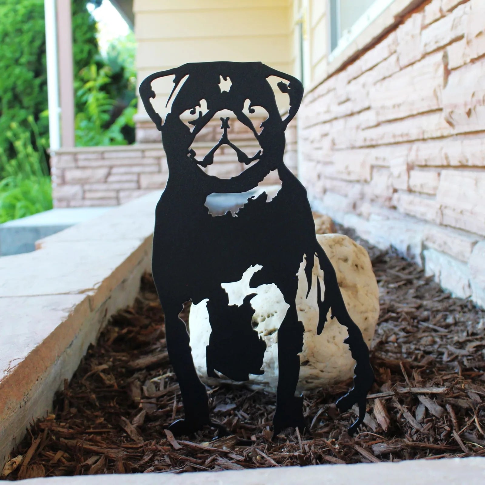 Black metal silhouette of a sitting pug, designed for outdoor decor, set against a mulch background.