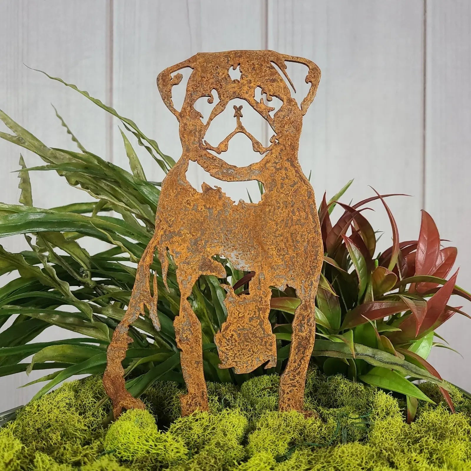 Pug silhouette in rusted Corten steel, surrounded by vibrant greenery and moss, perfect for outdoor decor.