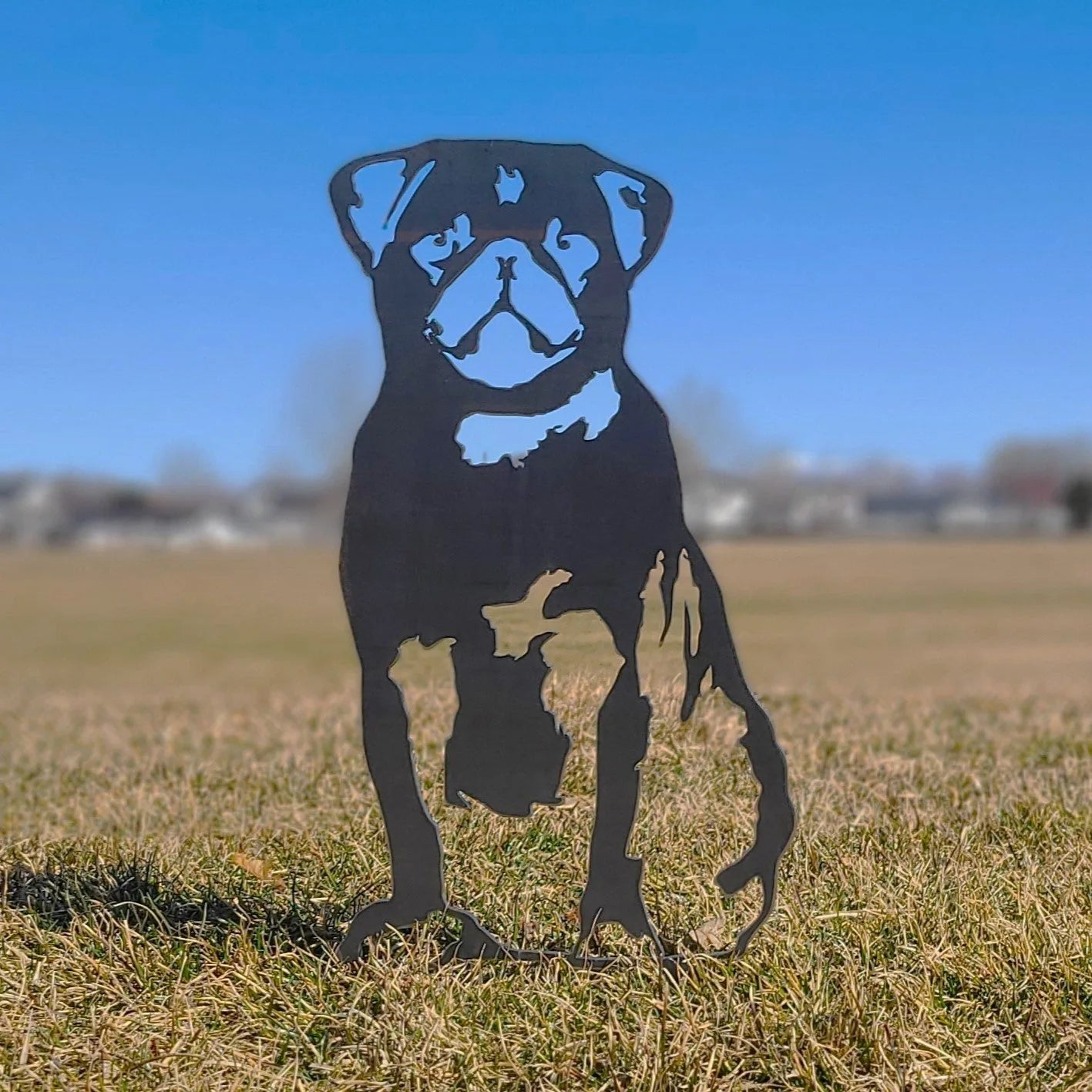Black metal silhouette of a seated pug against a clear blue sky, showcasing intricate details of the dog's features.