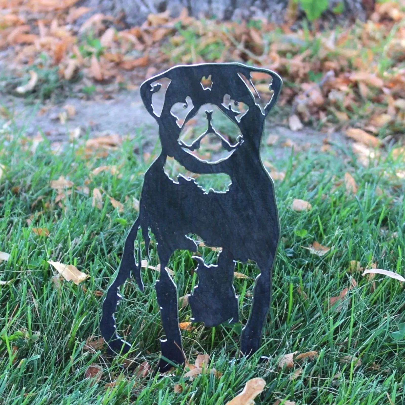 Black metal silhouette of a seated pug dog on green grass, perfect for outdoor decor.
