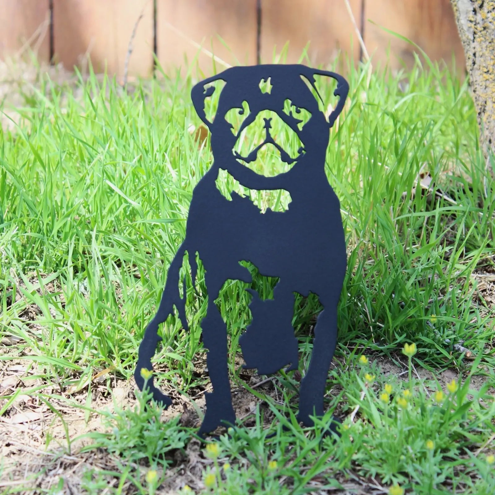 Black metal silhouette of a seated pug stands in lush green grass, adding dog-themed decor to an outdoor space.