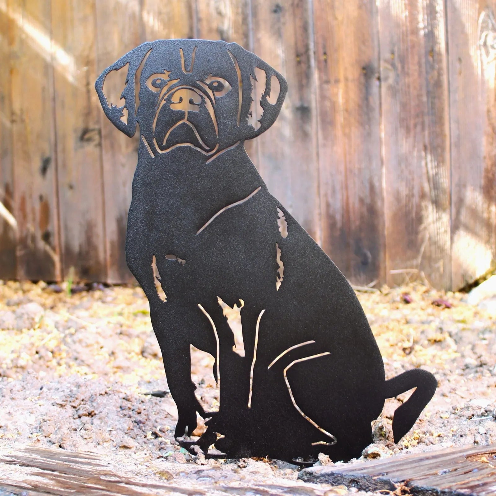 Black metal silhouette of a Puggle sitting, showcasing intricate cutouts, against a rustic wooden backdrop.
