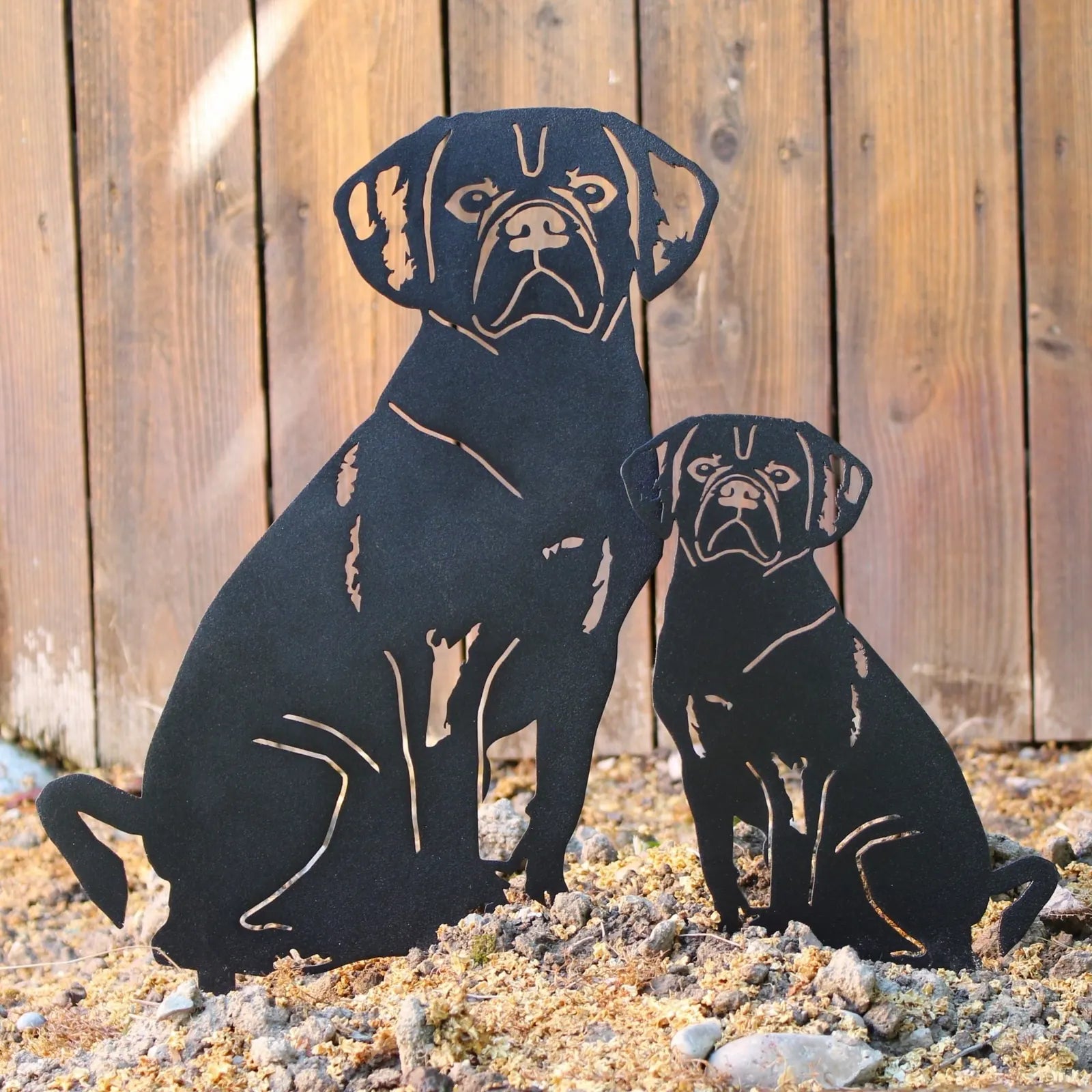 Black metal silhouette of a puggle dog standing next to a smaller silhouette, set against a rustic wood background.