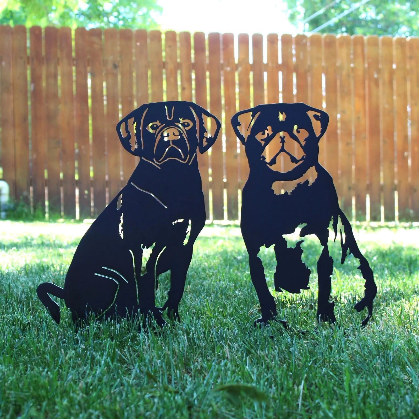 Black metal Puggle silhouette art, featuring two sitting dogs on grass, set against a wooden fence backdrop.