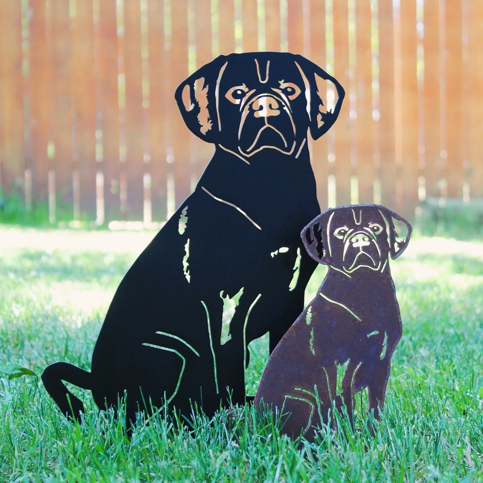 Black metal Puggle silhouette art standing beside rust patina version on grass, adding decorative charm to any garden.