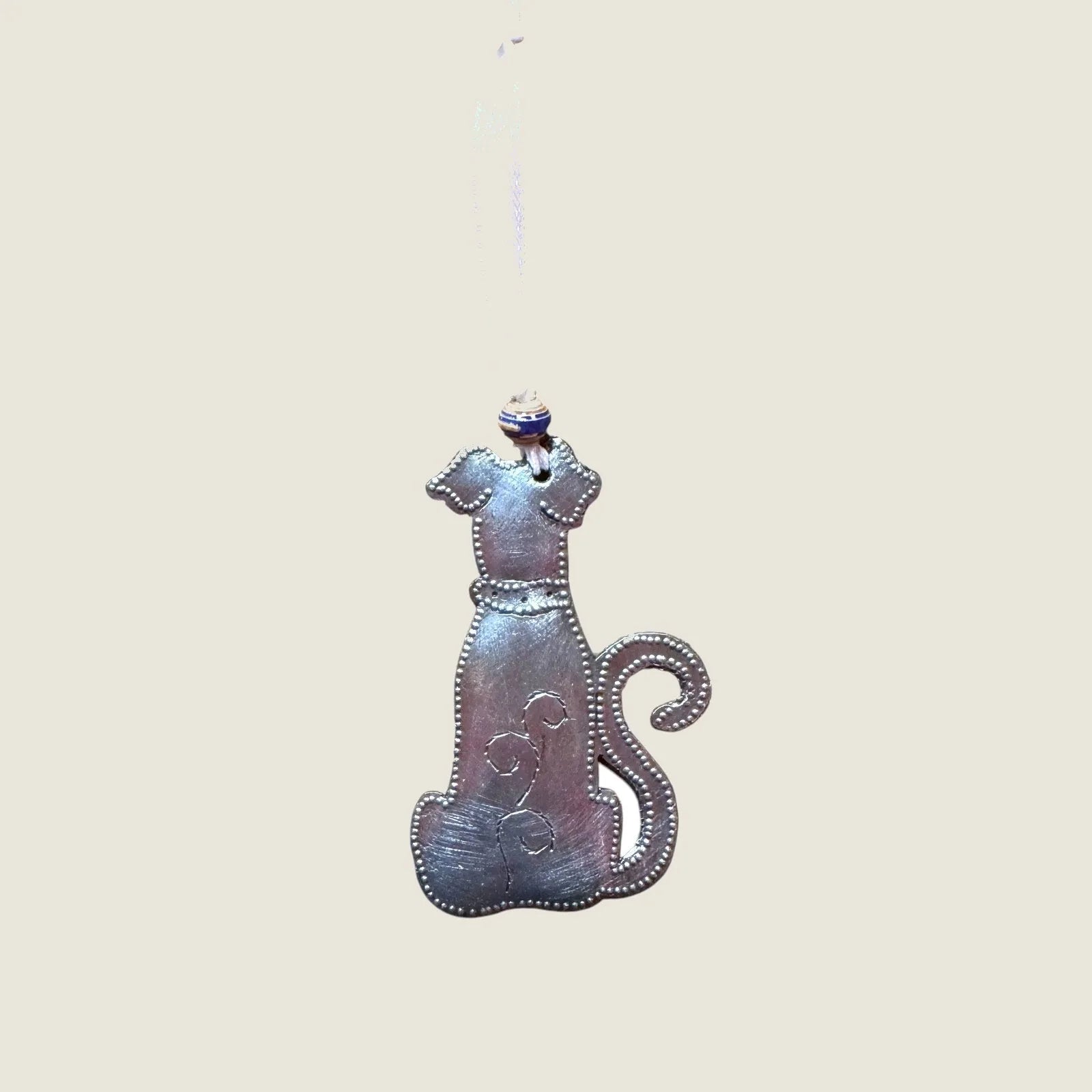 Handmade dog ornament featuring a steel drum design and paper bead, hung by a white ribbon, measuring 4x2 inches.