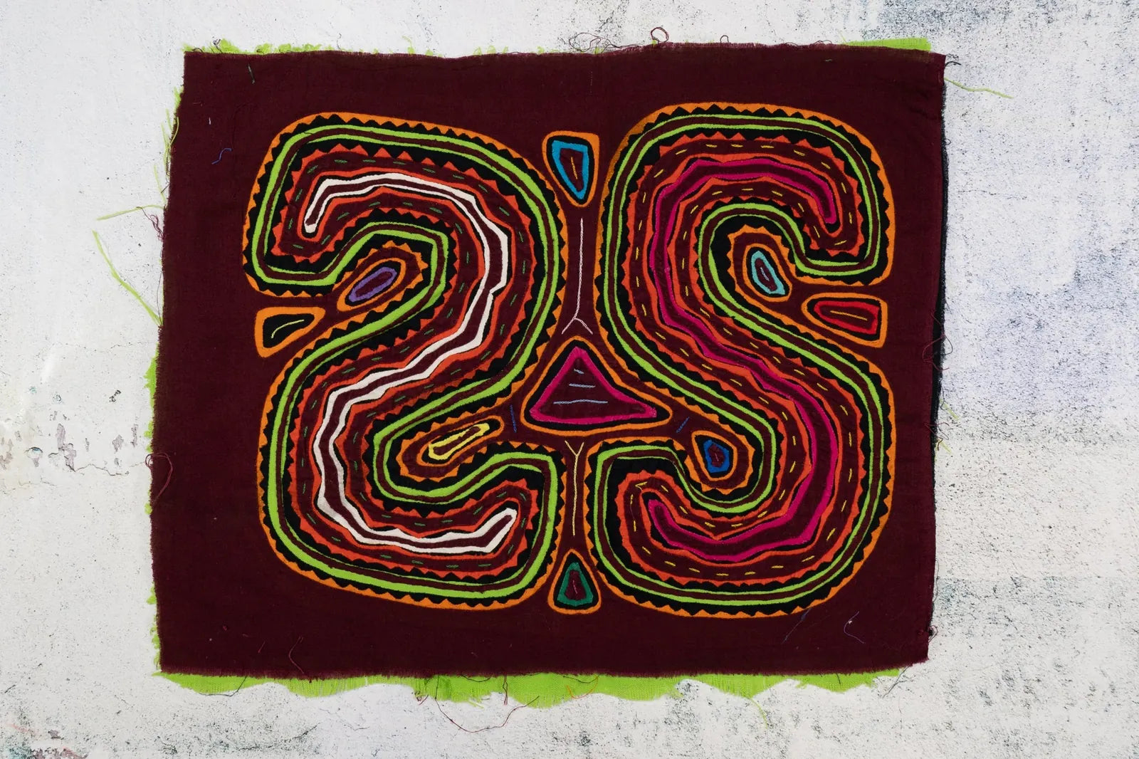 Colorful hand-stitched Mola tapestry featuring abstract shapes in maroon, green, orange, and pink, showcasing traditional...