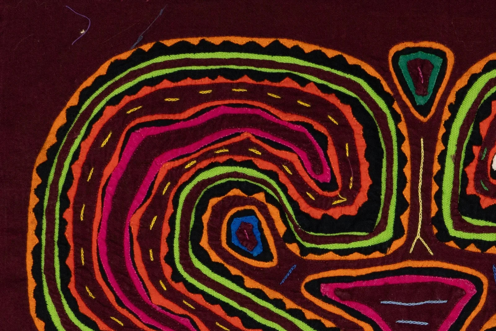 Colorful hand-stitched Mola tapestry features swirling patterns in pink, orange, green, and black against a rich maroon ba...
