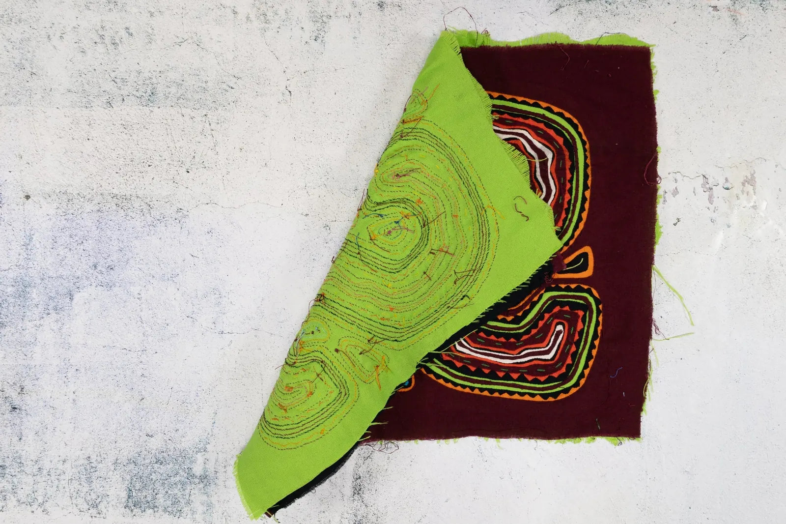 Colorful hand-stitched Mola tapestry featuring geometric patterns in green, burgundy, and earthy tones, showcasing artisan...