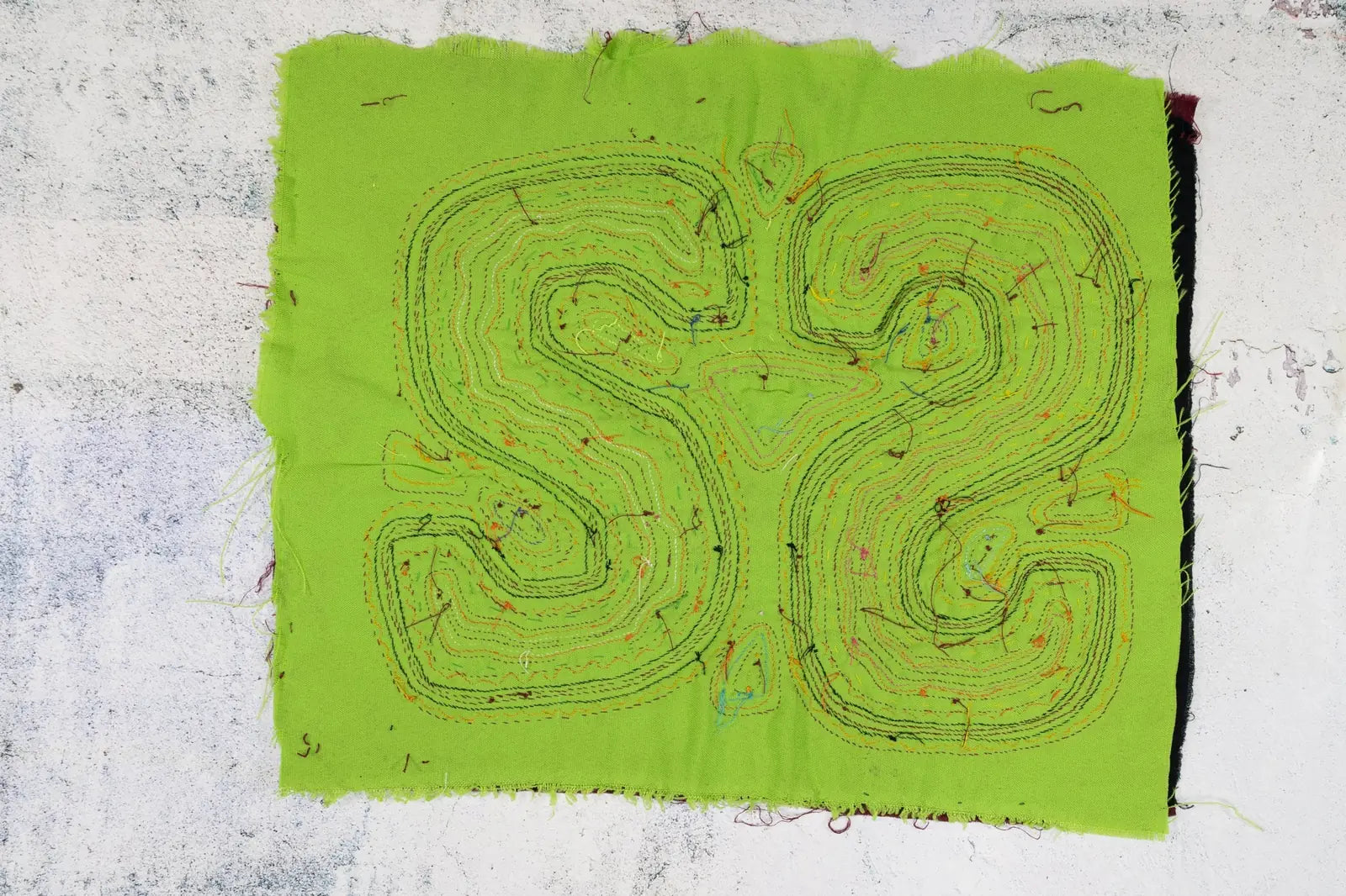 Bright green decorative tapestry featuring intricate black and multicolored stitching in a swirling pattern.