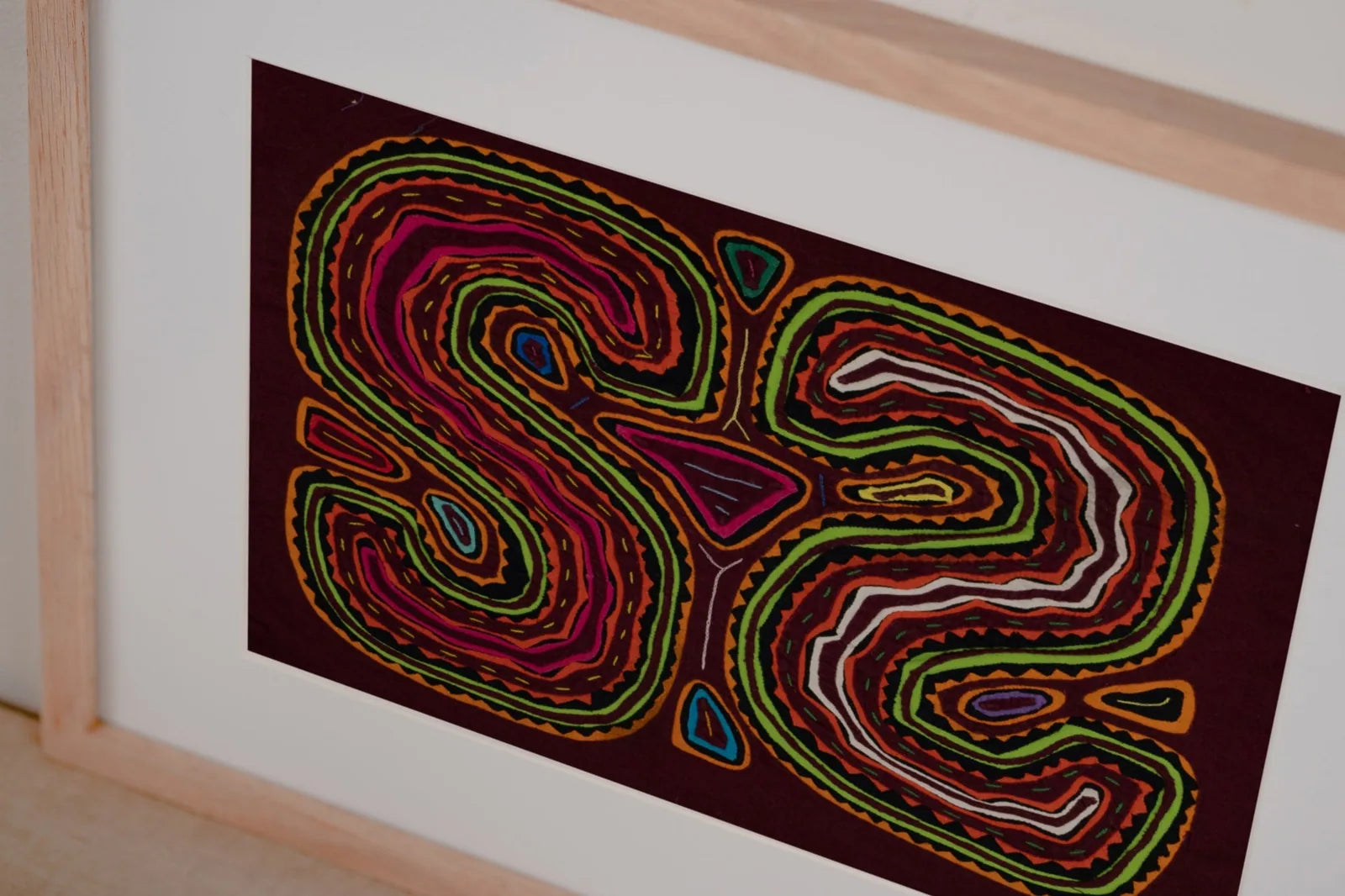 Vibrant hand-stitched Mola tapestry featuring intricate swirling designs in pink, green, and brown on a dark background.