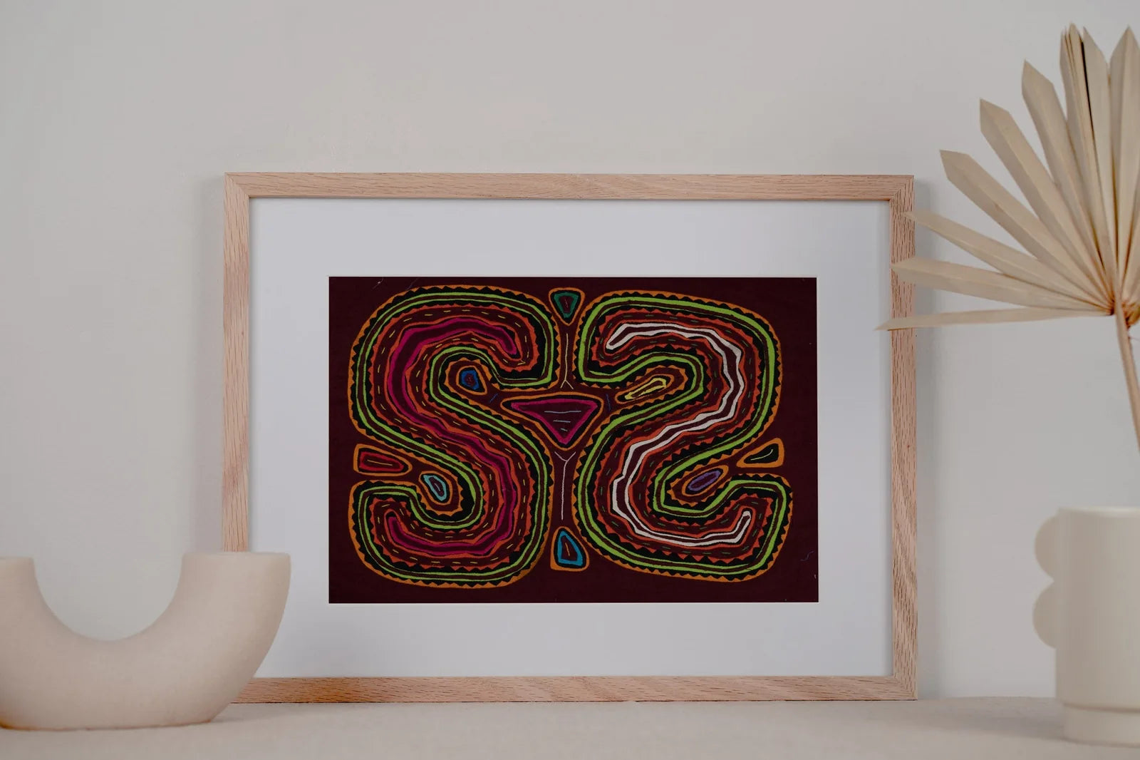 Hand-stitched Mola tapestry featuring vibrant pink, green, and blue geometric designs on a dark background.