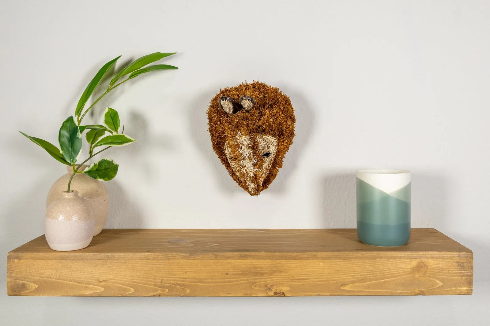 Handwoven Puppy Dog Mask in earthy browns on a wooden shelf, accompanied by vases and a candle, enhancing home decor.