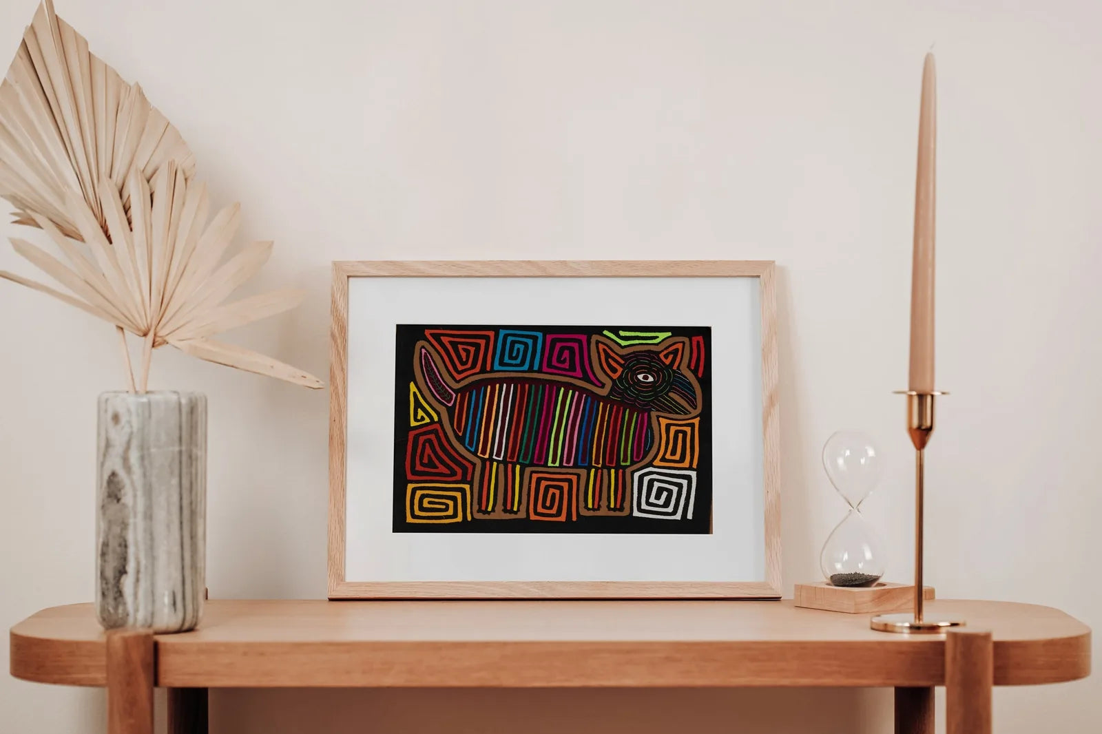 Colorful hand-stitched fabric art depicting a dog with geometric patterns, framed in wood and displayed on a shelf.