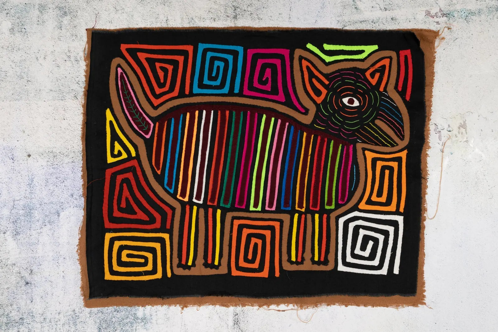 Colorful hand-stitched Mola featuring a dog design with bold lines and geometric patterns on a black background.