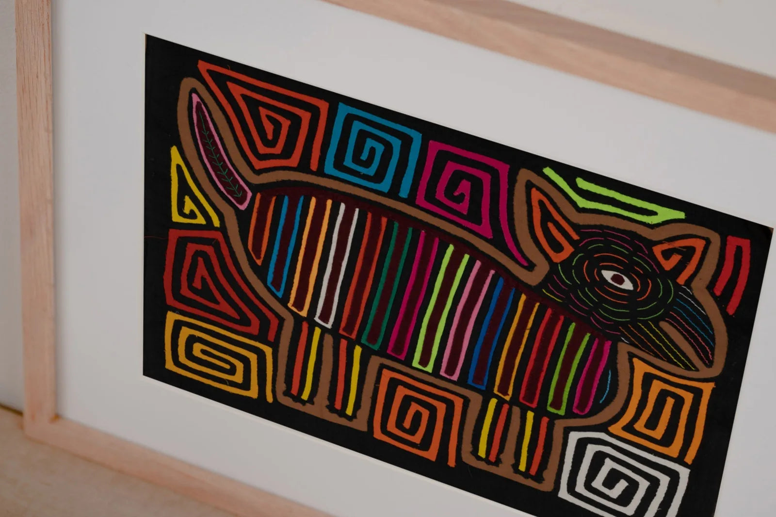 Colorful hand-stitched Mola featuring a dog design with vibrant stripes and intricate patterns, framed for display.