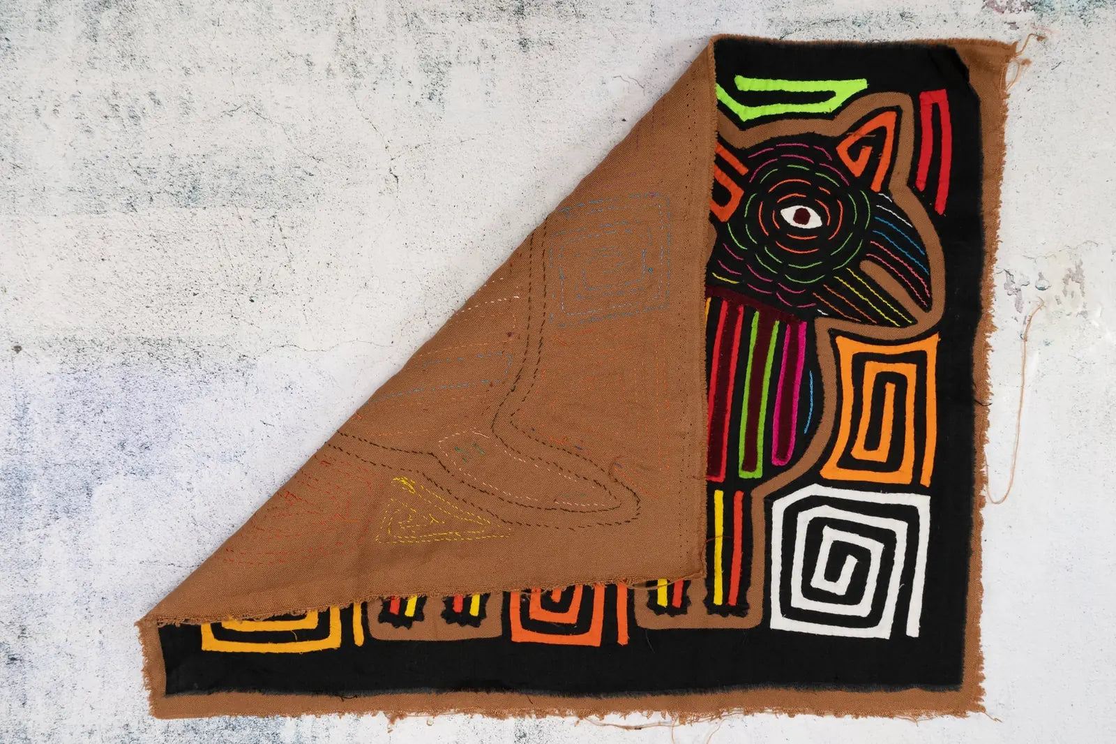 Colorful hand-stitched Mola textile featuring a dog design with bright geometric patterns on a black background.