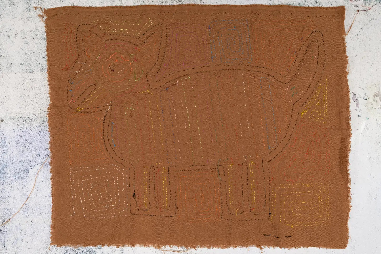 Hand-stitched brown textile featuring a dog design, embellished with colorful reverse appliqué stitching.