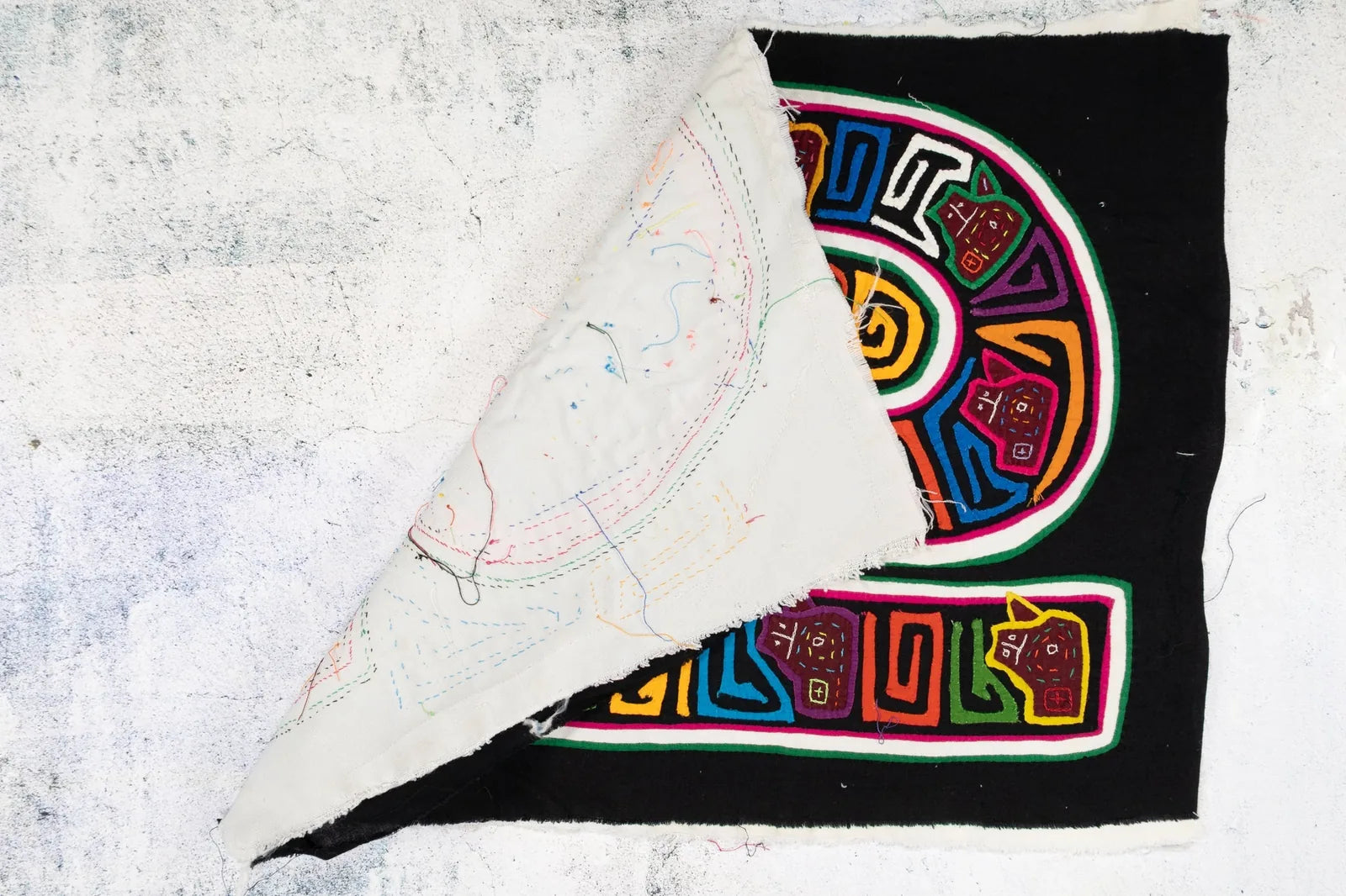 Colorful hand-stitched Mola textile featuring geometric designs on a black background, showcasing vibrant patterns.
