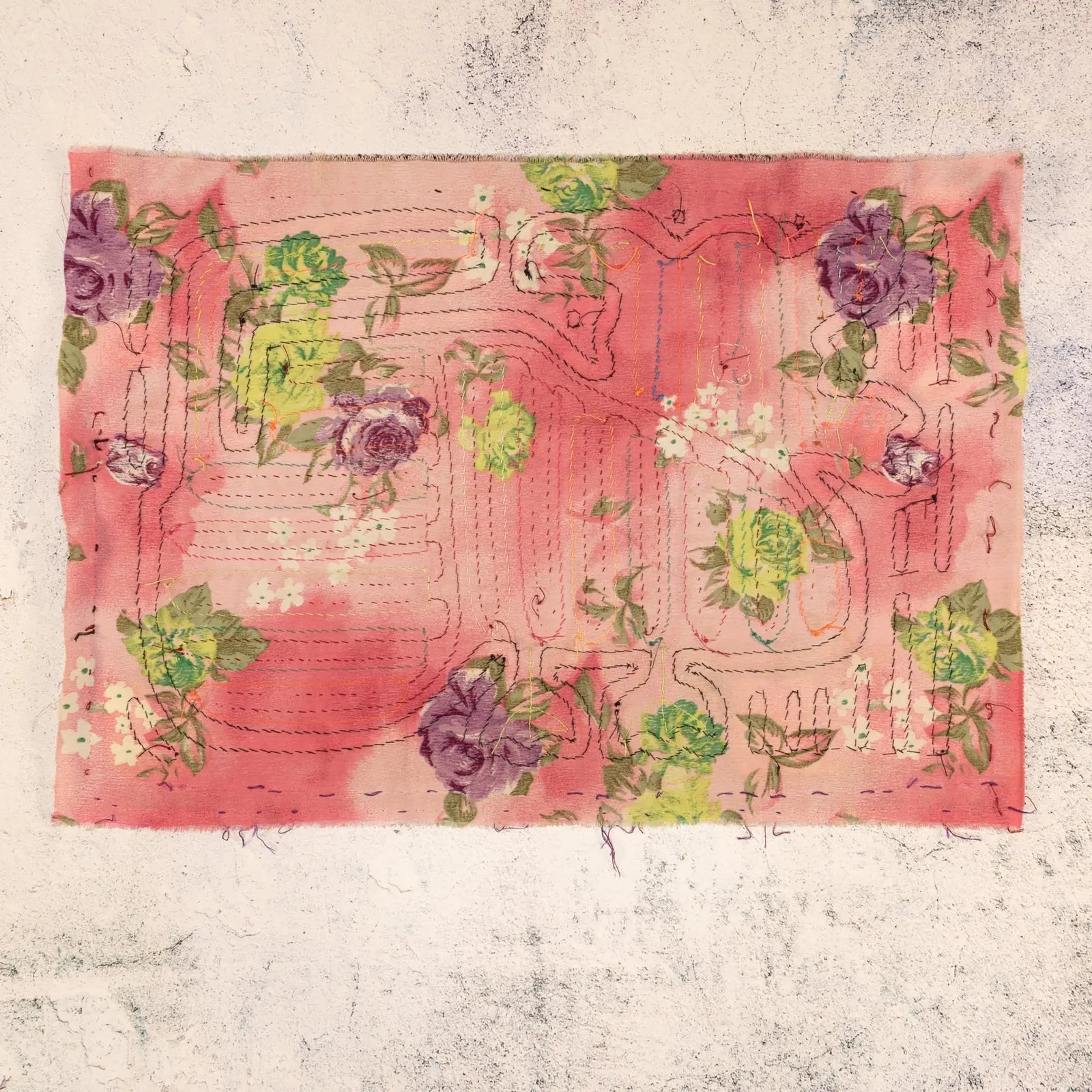 Hand-stitched decorative tapestry featuring floral designs in purple and green on a pink background.