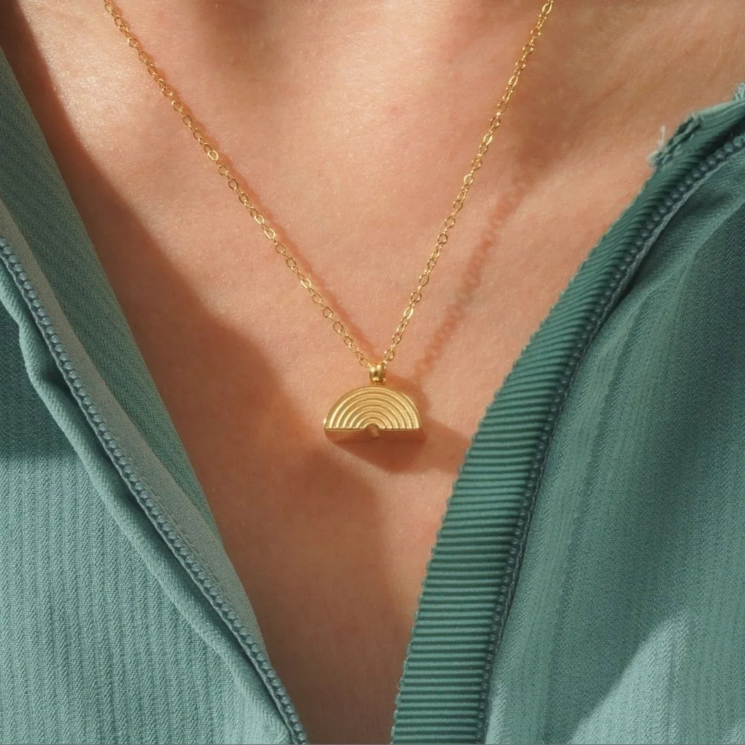 Gold rainbow bridge cremation necklace resting on a person's collarbone, showcasing its textured, half-moon design.