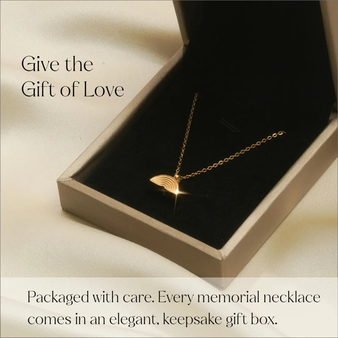 Gold cremation necklace with a rainbow design, elegantly displayed in a keepsake gift box on a soft fabric background.