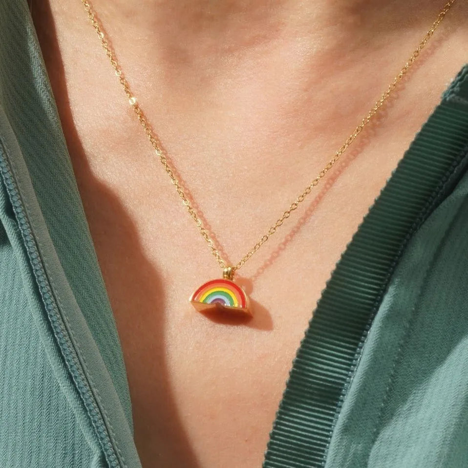 Gold necklace featuring a colorful hand-painted rainbow pendant resting on a person's chest, symbolizing pet memorial.
