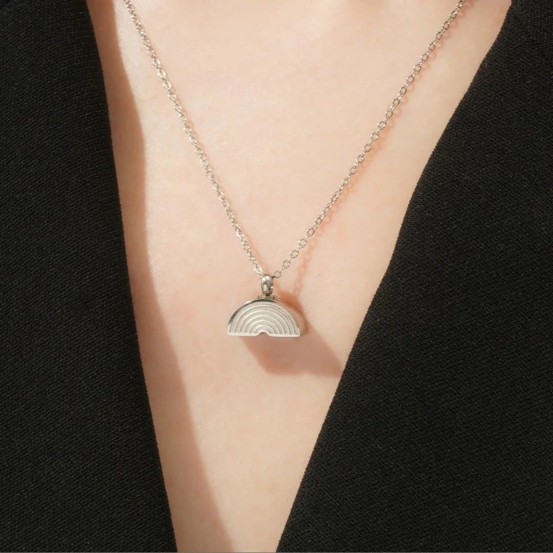 Silver Rainbow Bridge cremation necklace on a chain, resting on black fabric, symbolizing cherished pet memories.