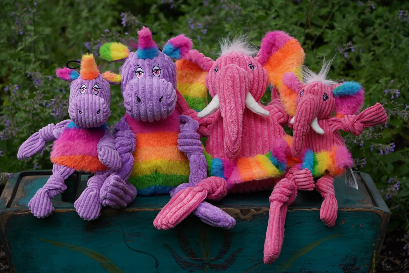 Colorful plush elephant and unicorn toys with knotted limbs, featuring vibrant rainbow patterns and smiling faces.