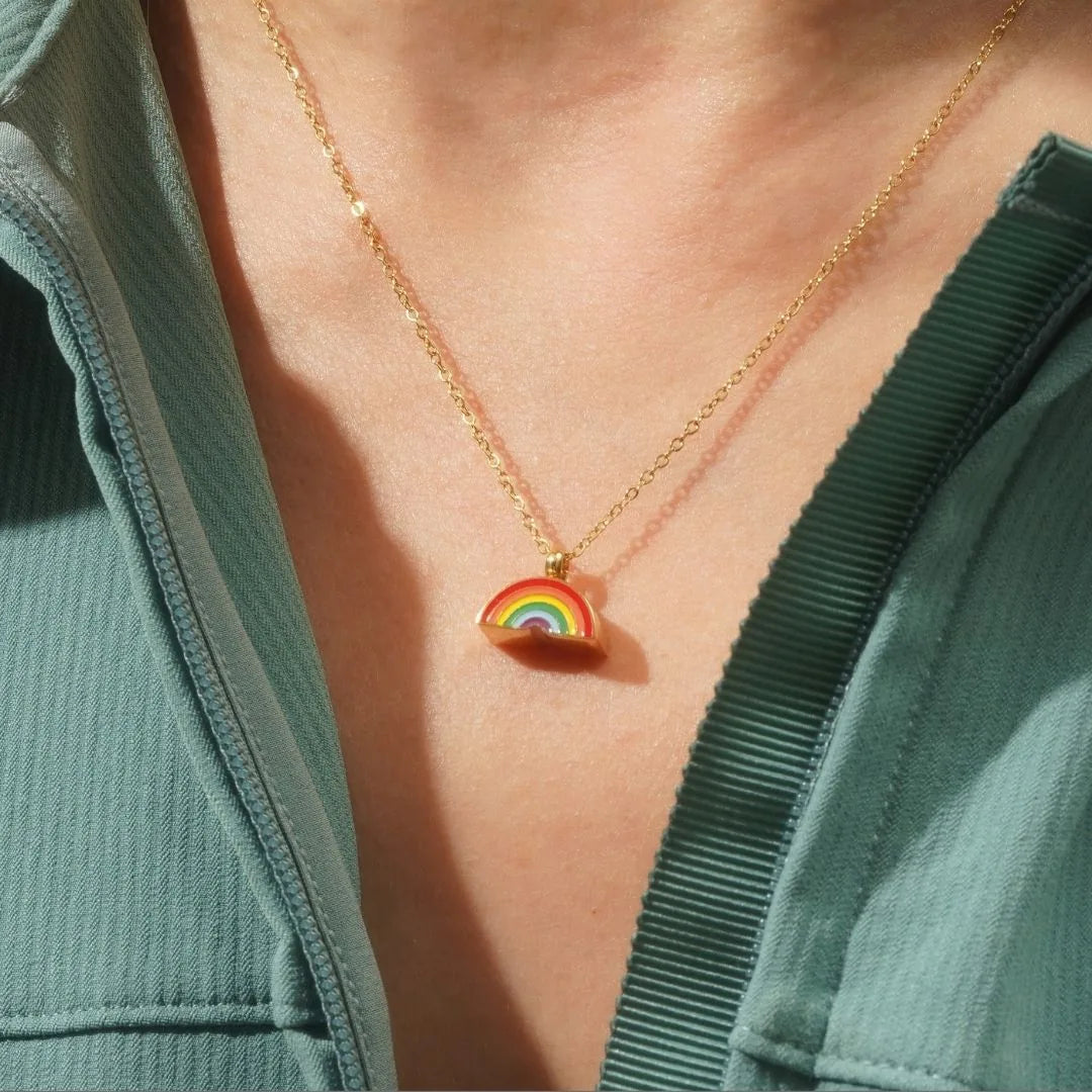 Colorful rainbow pendant necklace on a gold chain, worn against a textured green garment.