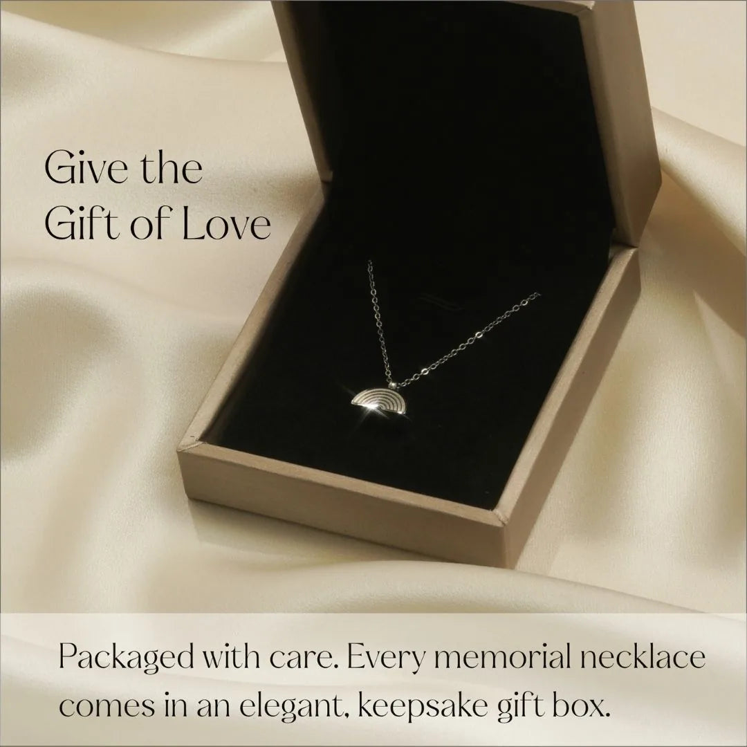 Silver rainbow pendant necklace displayed in an elegant gift box, resting on soft black fabric.