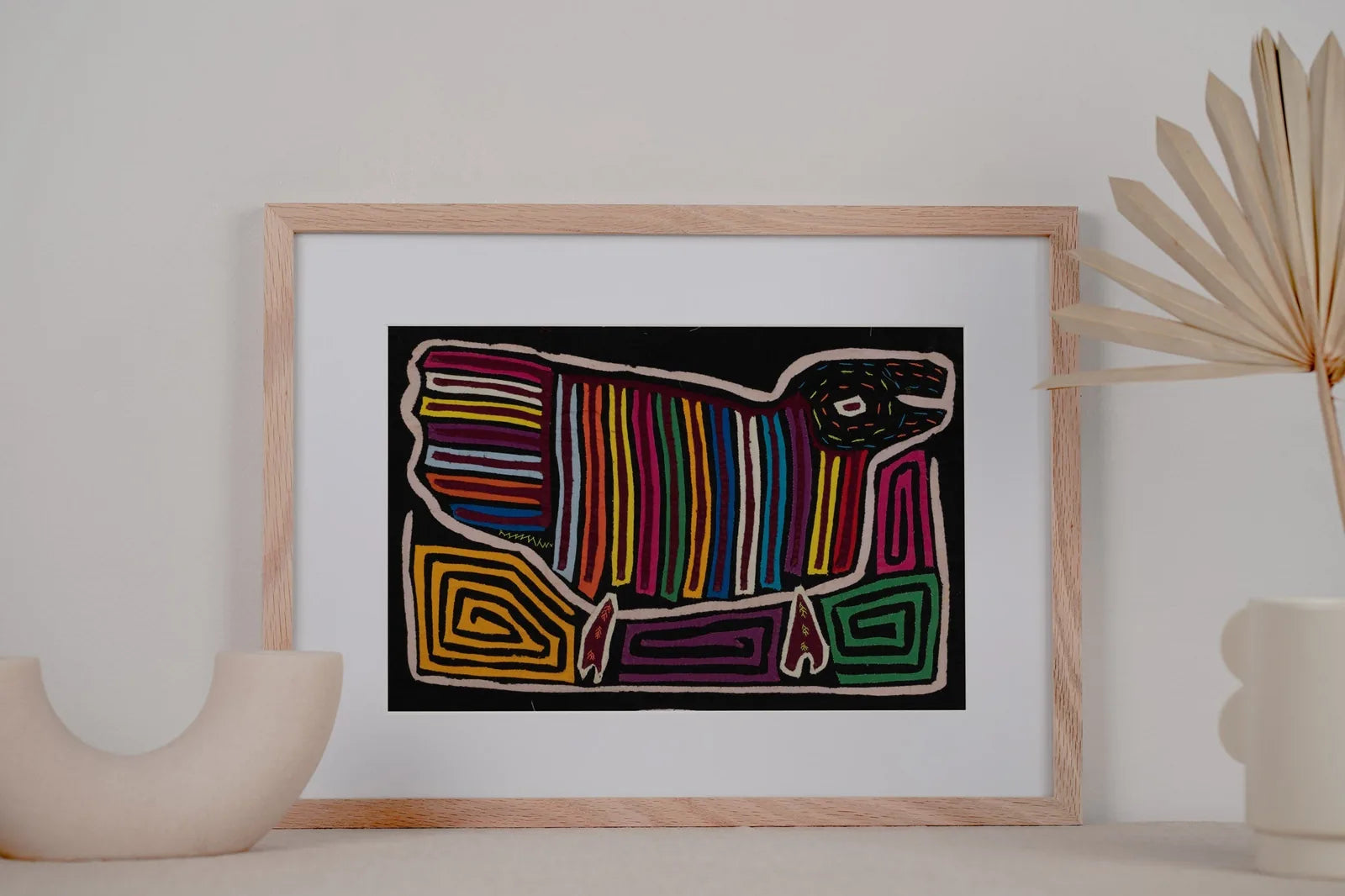 Hand-stitched Mola tapestry featuring a colorful striped dog design on a black background, framed in wood.