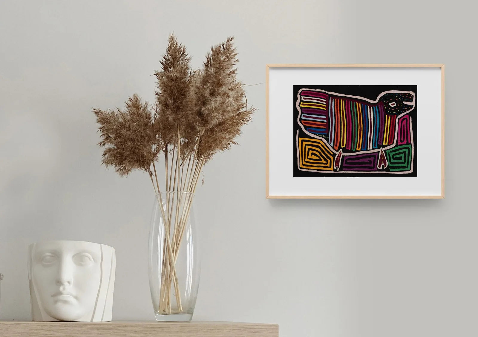 Colorful hand-stitched Mola of a dog in geometric patterns, framed against a neutral wall with decorative elements.