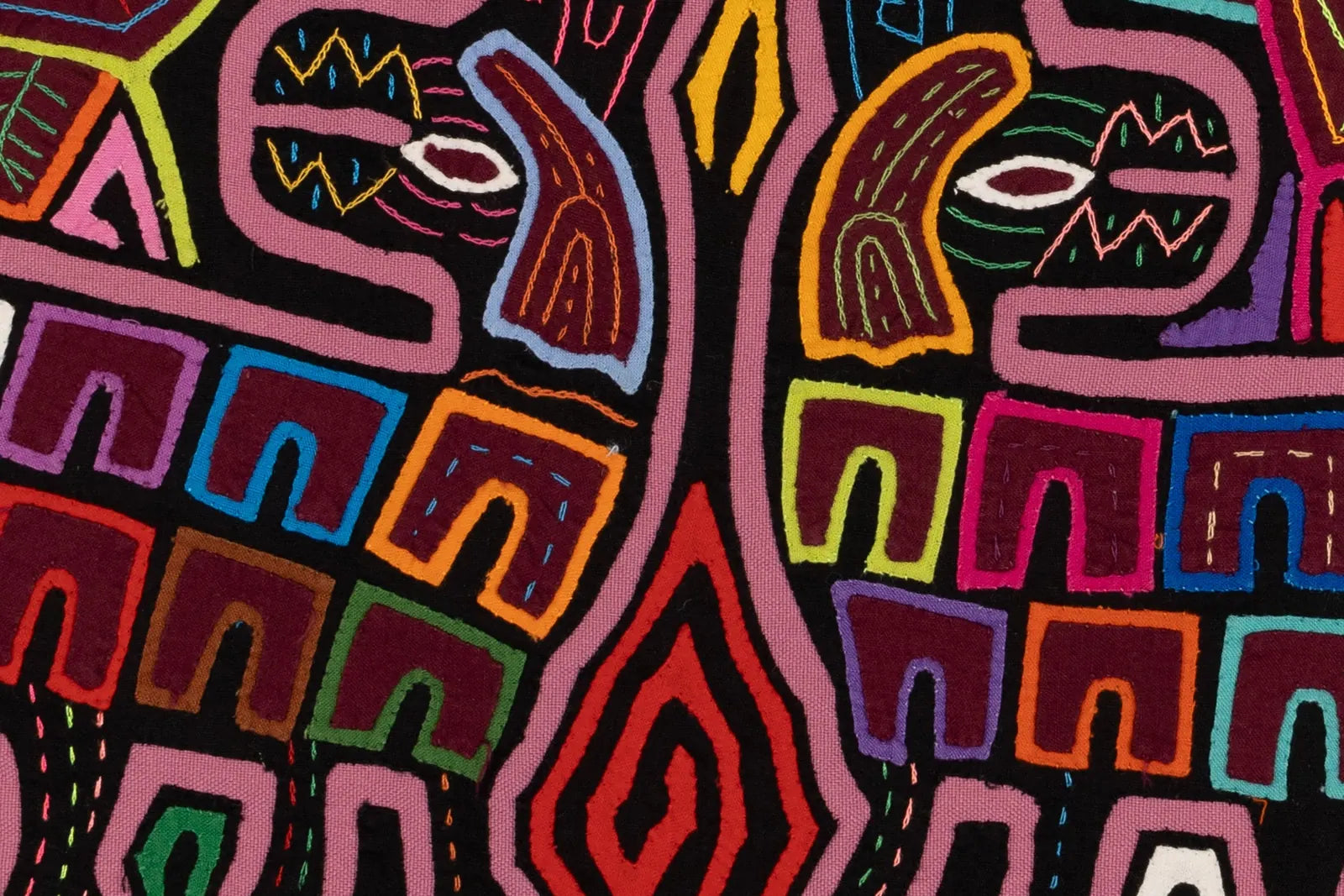 Colorful geometric patterns with intricate stitching on a handcrafted Mola textile featuring a black background.