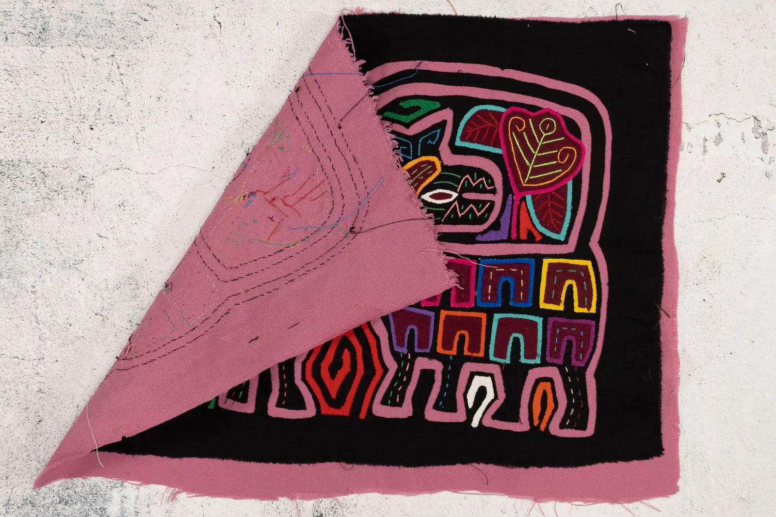 Colorful geometric patterns stitched on black fabric, revealing a pink backing in this handcrafted Panama mola tapestry.