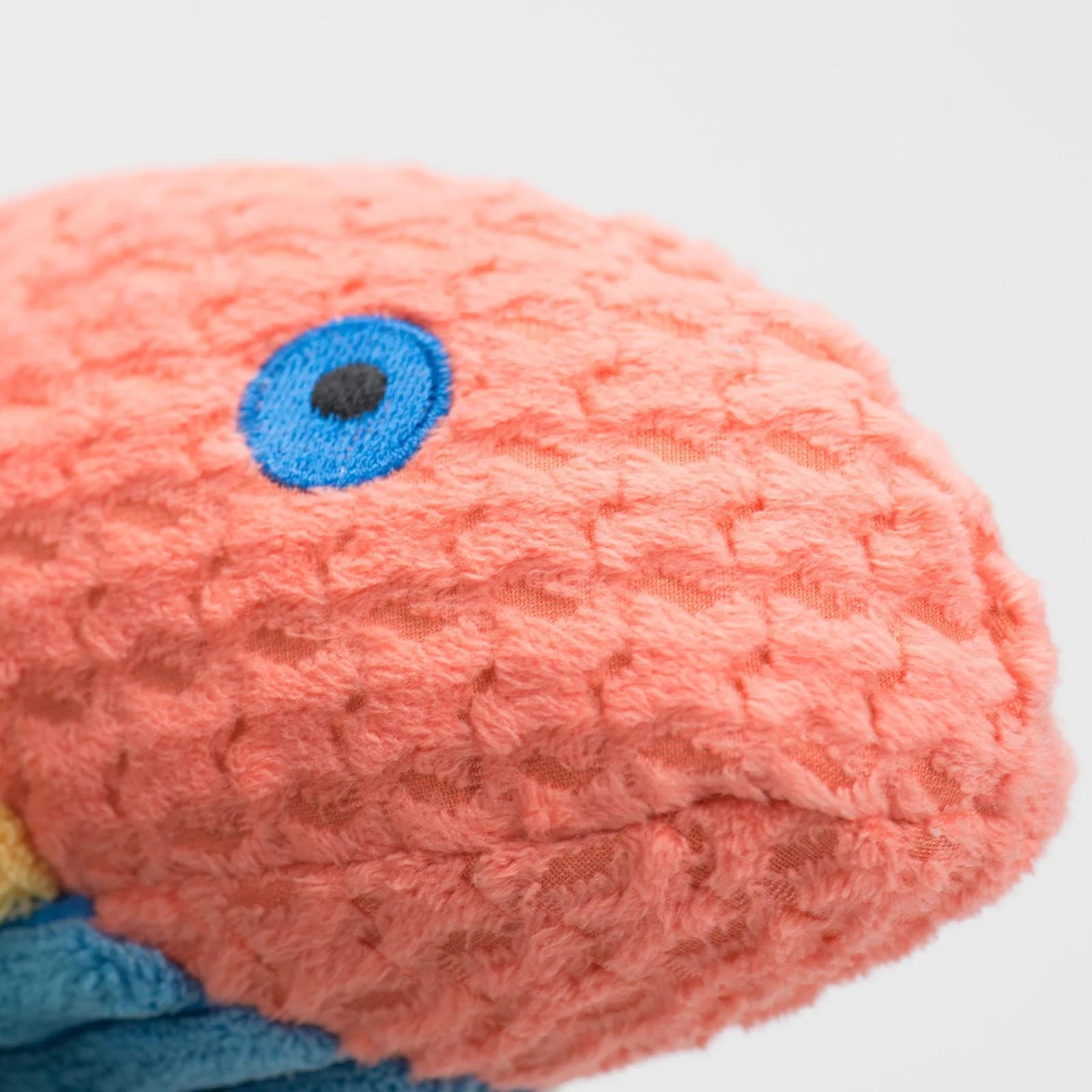Textured plush dog toy in coral and blue, featuring a whimsical fish design with embroidered eyes.